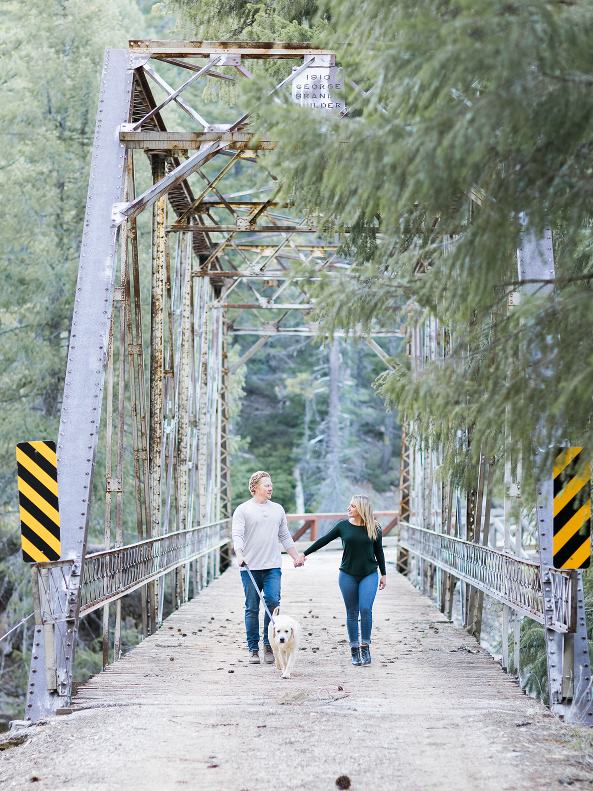 a couple and their dog walk across a bridge during their mountain engagement photos